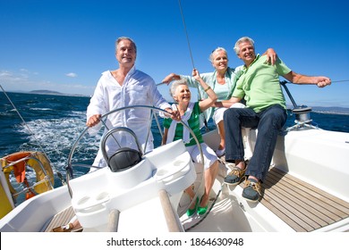 Two senior couples sailing out at sea on a bright, sunny day while one man is standing at the helm and steering the yacht