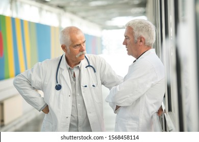 Two Senior Doctors Talking In Hospital Corridor