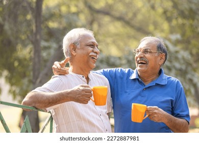 Two senior friends having fun raising a toast with coffee cups at park - Powered by Shutterstock