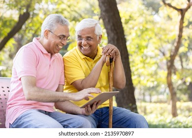 Two Senior Male Friends Watching Social Media Content On Digital Tablet At Park
