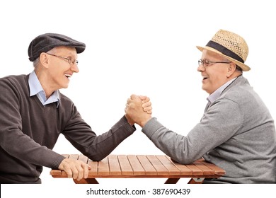 Two Senior Man Having An Arm Wrestle Competition Seated At A Table Isolated On White Background