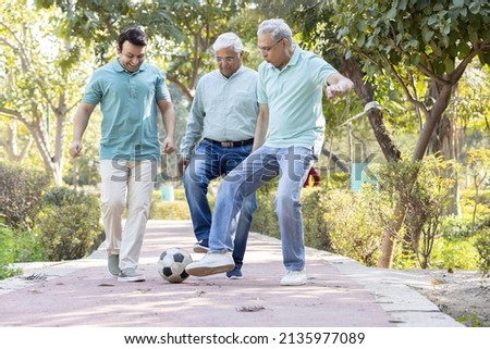 Two senior man with son having fun while playing football at park
