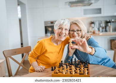 two senior mature women caucasian female woman friends or sisters play leisure chess board game at home have fun spend time together at home bright photo copy space - Powered by Shutterstock