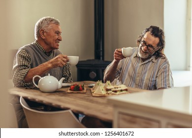 Two senior men having tea cups while sitting together at table indoors. Retired men enjoying tea and snacks together at home. - Powered by Shutterstock