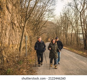 Two Senior Men And One Woman Taking A Walk Along River Bluffs In Midwest On Cool Day; Two People Walking With Hiking Poles