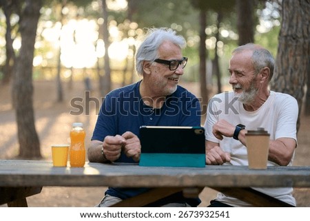Two senior men using tablet and talking in park