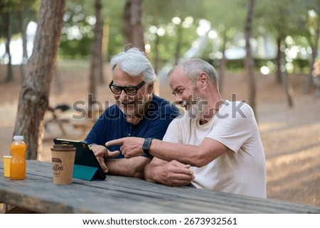 Two senior men using a tablet in a park, sharing moments and staying connected