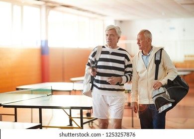 Two Senior Sportsmen With Bags Having Talk While Moving To Their Tennis Table