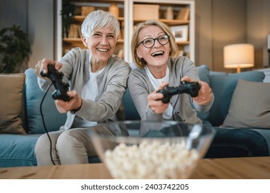 Two senior women caucasian friends or sisters happy old siblings pensioner playing video game console using joystick or controllers while sitting at home real people family leisure concept copy space - Powered by Shutterstock