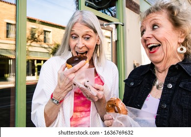 Two Senior Women Eating Donuts And Laughing