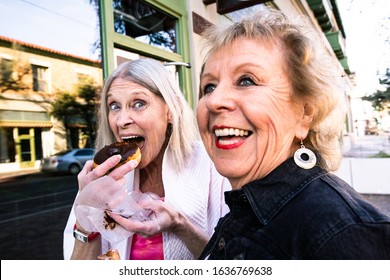 Two Senior Women Eating Donuts Outdoors And Laughing