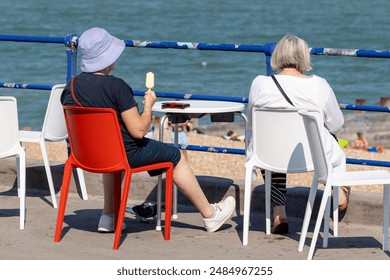 Two senior women enjoying the sun and ice cream on a seaside promenade - Powered by Shutterstock