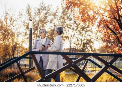 Two senior women or friends drinking coffee walking along park - Powered by Shutterstock