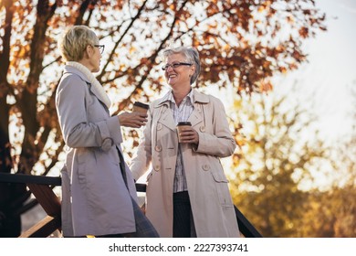 Two senior women or friends drinking coffee walking along park - Powered by Shutterstock