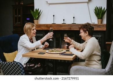 Two Senior Women Friends Having Dinner At Restaurant, Attractive Lady Spending Time Together Indoors. Old Friends Drinking Wine In Modern Apartment.