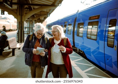 Two senior women laughing and checking train tickets at station - Powered by Shutterstock