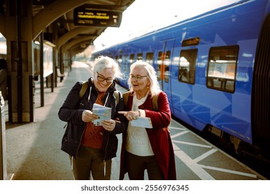 Two senior women laughing and checking train tickets at station - Powered by Shutterstock