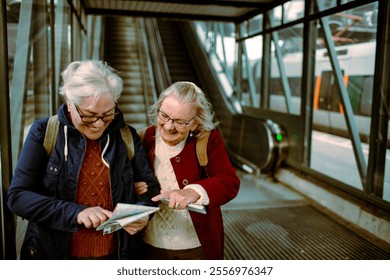 Two senior women laughing and checking train tickets at station - Powered by Shutterstock