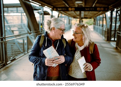 Two senior women laughing and checking train tickets at station - Powered by Shutterstock