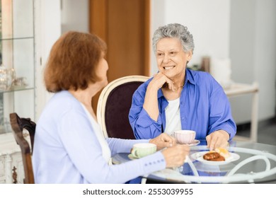 Two senior women share a joyful conversation at a cafe table, sipping tea and savoring snacks. Their relaxed demeanor reflects the joy of companionship during retirement. - Powered by Shutterstock