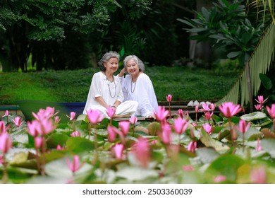 Two senior women sitting together by a lotus pond, enjoying each other's company and the serene garden surroundings, smiling and relaxed. - Powered by Shutterstock