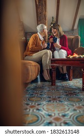 Two Senior Women Talking, Drinking Coffee And Enjoying Christmas Together At Home