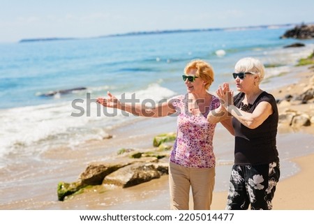 Two senior women are walking along the rocky shore, talking and laughing, having a pleasant time together