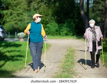 Two Senior Women Wearing Medical Masks Walking With Nordic Walking Poles During Covid-19 Pandemic