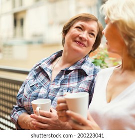 Two Seniore Women Drinking Coffee On Balcony And Smiling