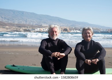 two seniors and mature people sitting on a surfboard on the sand at the beach with sea and waves at the background - couple of active pensioner preparing to enter at the water - Powered by Shutterstock