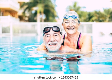 two seniors or mature people together hugged in the blue water of the swimming pool - active woman and man doing exercise together - summertime and having fun