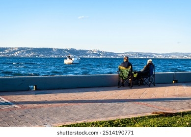 Two seniors sitting by the seaside watching a boat on the horizon, quite evening in Kocaeli, Turkey - Powered by Shutterstock