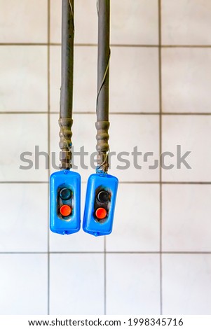 Two Separate Remote Control Panels Hanged On Long Rubber Holders Against White Tiles Wall. Vertical Image