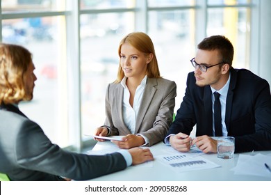 Zwei ernsthafte Geschäftspartner, die jungen Männern bei ihrem Treffen im Büro aufmerksam zuhören