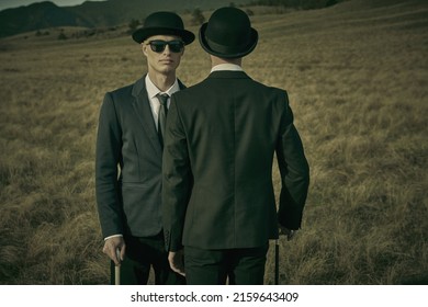 Two serious calm men in black suits, bowler hats and black sunglasses stand facing each other in an open wild field. Surrealist style.