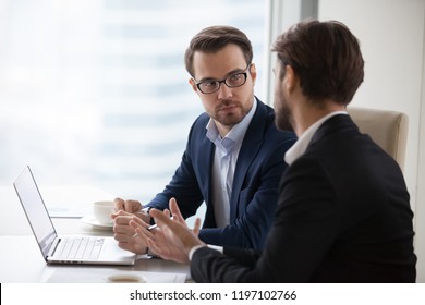Two serious caucasian men in suits discussing or planning business issues in the office. Colleagues or client and consultant are sitting at the table next to each other and talking.