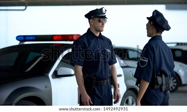 Two serious police officers communicating on\
parking lot, patrolling\
district