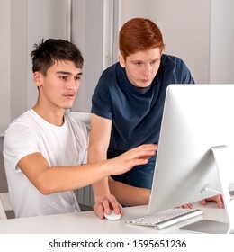 Two Serious Teenager Guys Are Using  Computer And Discussing Something 