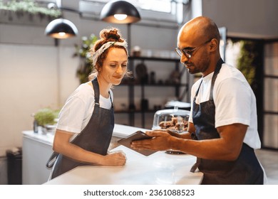 Two service professionals in the hospitality industry use a tablet device to efficiently manage orders and ensure customer satisfaction. Tech savvy waitstaff members working as a team in a cafe.