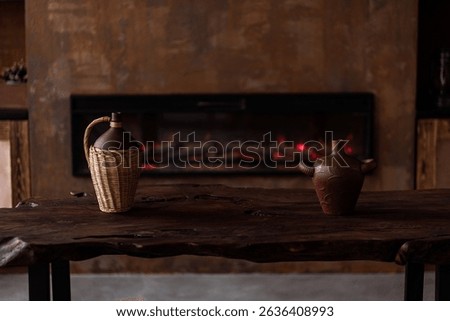 two sheared jugs stand on a wooden table against a fireplace 