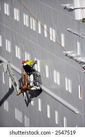 Two Shipyard workers isolated on platform paint huge ferry ship in dry dock