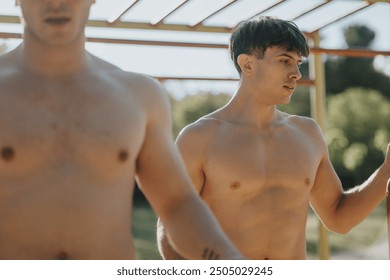 Two shirtless men are seen exercising at an outdoor jungle gym on a sunny day, demonstrating fitness and strength. - Powered by Shutterstock