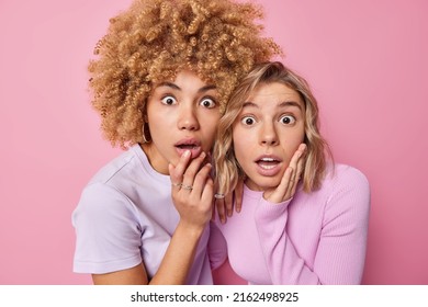 Two shocked women friends stare impressed or startled at camera feel concerned gasp from wonder and fear dressed casually stand next to each other isolated over pink background. Omg concept.