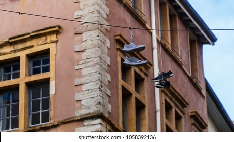 Two shoes dangling from a cable in front of an old antique mediterranean building in Lyon