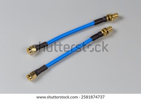Two short blue high-frequency cable adapters with yellow coaxial threaded connectors on the edges on a gray surface