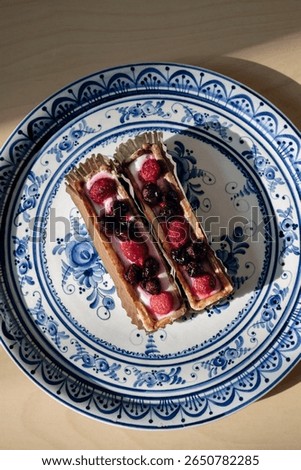 Two shortbread baskets with cream and berries on a plate painted with traditional blue Gzhel. View from above on a sunny day with hard shadows.