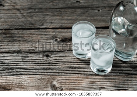 Two shot glasses with cold vodka or gin on wooden table,