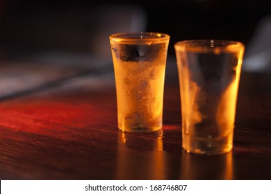 Two Shot Glasses Of Vodka On A Wooden Table.