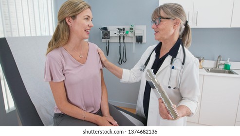 Two shot of woman talking to her reassuring primary care doctor in exam room. Middle aged patient having appointment with female senior physician