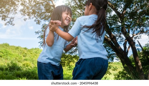 Two Sibling Little Girls Laughing And Hugging Each Other On Warm And Sunny Summer Day In The Garden. Young Girls With Her Mother Spending Day In Park.